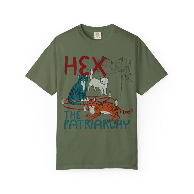 Puede incluir: Camiseta verde oliva con un dise&ntilde;o gr&aacute;fico que presenta tres gatos, una telara&ntilde;a y el texto "HEX THE PATRIARCHY" en rojo y azul. Los gatos est&aacute;n en varios colores y poses, con velas y un dise&ntilde;o de pentagrama.