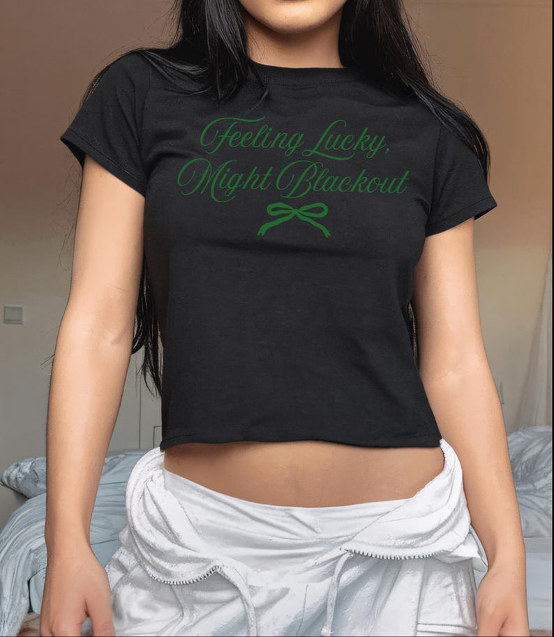 May include: Black crop top with the text "Feeling Lucky, Might Blackout" in green script. A green bow graphic is below the text. The shirt is short-sleeved and made of a soft material.