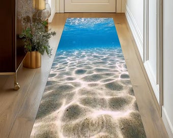 May include: A rectangular runner rug featuring an underwater ocean scene. The rug displays a blue ocean surface above and a sandy seabed below, creating a serene and aquatic ambiance. The design is printed on a rectangular rug.