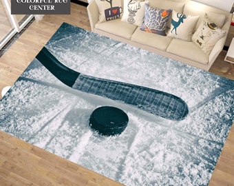 Puede incluir: Una alfombra de hockey azul y blanca con un palo de hockey y un disco sobre una superficie nevada.