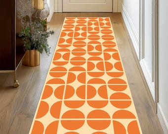 May include: A rectangular runner rug with a geometric pattern of orange semi-circles on a cream background. The rug is placed in a hallway with wooden flooring and a white door.
