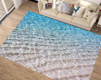 May include: A blue and white area rug with a design of rippling water over a sandy beach.