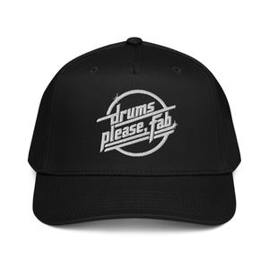 Puede incluir: Gorra de béisbol negra con visera curva. La gorra presenta el texto bordado "drums please, fab" en blanco, con una fuente estilizada dentro de un círculo blanco. Gorra clásica y ajustable.