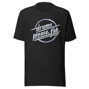 Könnte beinhalten: Dunkelgraues T-Shirt mit dem Text "drums please, fab" in silberner, stilisierter Schrift. Der Text befindet sich in einem silbernen Kreis mit Sternen-Effekt. Das T-Shirt hat kurze Ärmel.