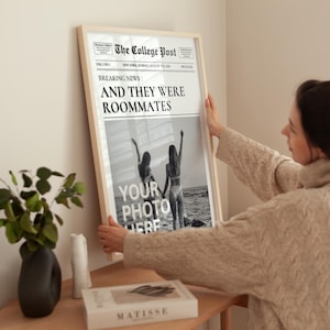 May include: A framed black and white photograph of two people standing on a beach. The photo is in a newspaper style frame with the headline "BREAKING NEWS: AND THEY WERE ROOMMATES".
