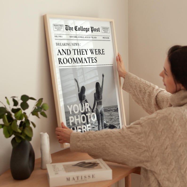 May include: A framed black and white photograph of two people standing on a beach. The photo is in a newspaper style frame with the headline "BREAKING NEWS: AND THEY WERE ROOMMATES".