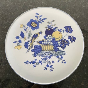 May include: A white ceramic plate with a blue and yellow floral design featuring a bird, grapes, and a basket of fruit.