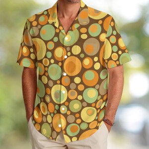 Puede incluir: Camisa de manga corta con un estampado retro de círculos coloridos en tonos marrón, amarillo, naranja y verde. La camisa tiene un cuello clásico y un corte relajado, perfecta para el uso diario. La camisa está hecha de una tela ligera.