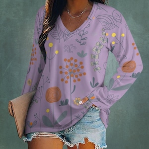 May include: A lavender V-neck long-sleeved shirt with a floral design. The pattern includes orange, yellow, and grey flowers and leaves. This casual top is suitable for everyday wear. The shirt is a comfortable, relaxed fit.