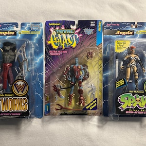 May include: Three action figure packages with the characters Vampire, Angela, and a blue character from the Total Chaos line. The packages are all from the Wetworks and Spawn lines. The packages are all in the same style with a white background and a black border.
