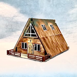 Könnte beinhalten: Ein Holzmodell einer kleinen A-förmigen Hütte mit einem braunen Dach, zwei Fenstern und einer Tür. Die Hütte hat eine kleine Veranda mit einem Geländer.