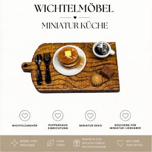 Könnte beinhalten: Ein Miniatur-Küchenset auf einem strukturierten Holzbrett mit einem Stapel Pfannkuchen mit Butter, einer kleinen Tasse mit dunkler Flüssigkeit, einem schwarzen Löffel und einer Gabel sowie zwei kleinen Lebensmitteln. Text WICHTELMÖBEL MINIATUR KÜCHE.