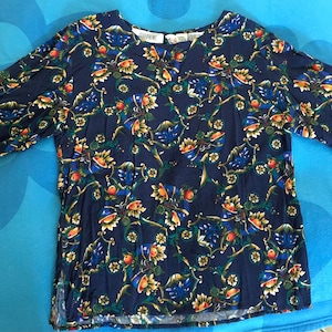 May include: A navy blue short-sleeved shirt with a floral print featuring yellow, orange, green, and blue flowers. The shirt has a round neckline and a relaxed fit.