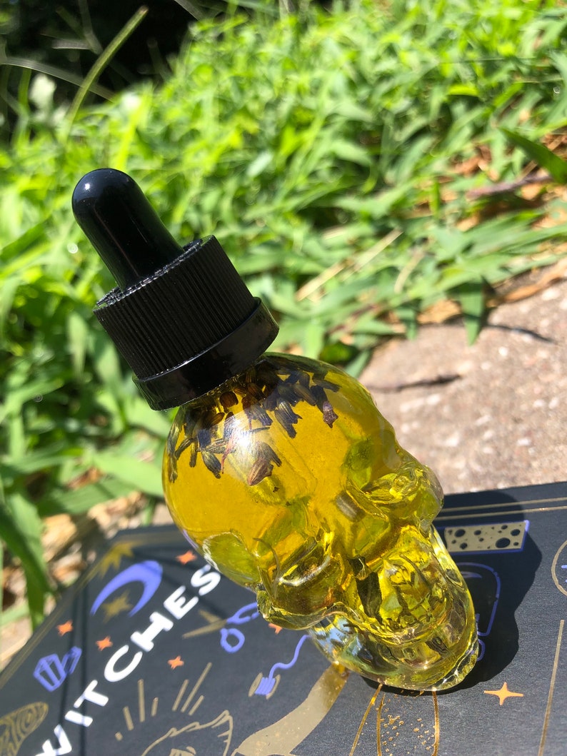 Peut inclure: Une bouteille en verre transparente en forme de cr&acirc;ne remplie d'un liquide jaune et d'herbes s&eacute;ch&eacute;es. La bouteille a un bouchon compte-gouttes noir.
