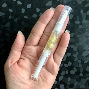 Peut inclure: Un tube en plastique transparent avec un bouchon blanc et un liquide jaune &agrave; l'int&eacute;rieur. Le tube est rempli de petites fleurs blanches.