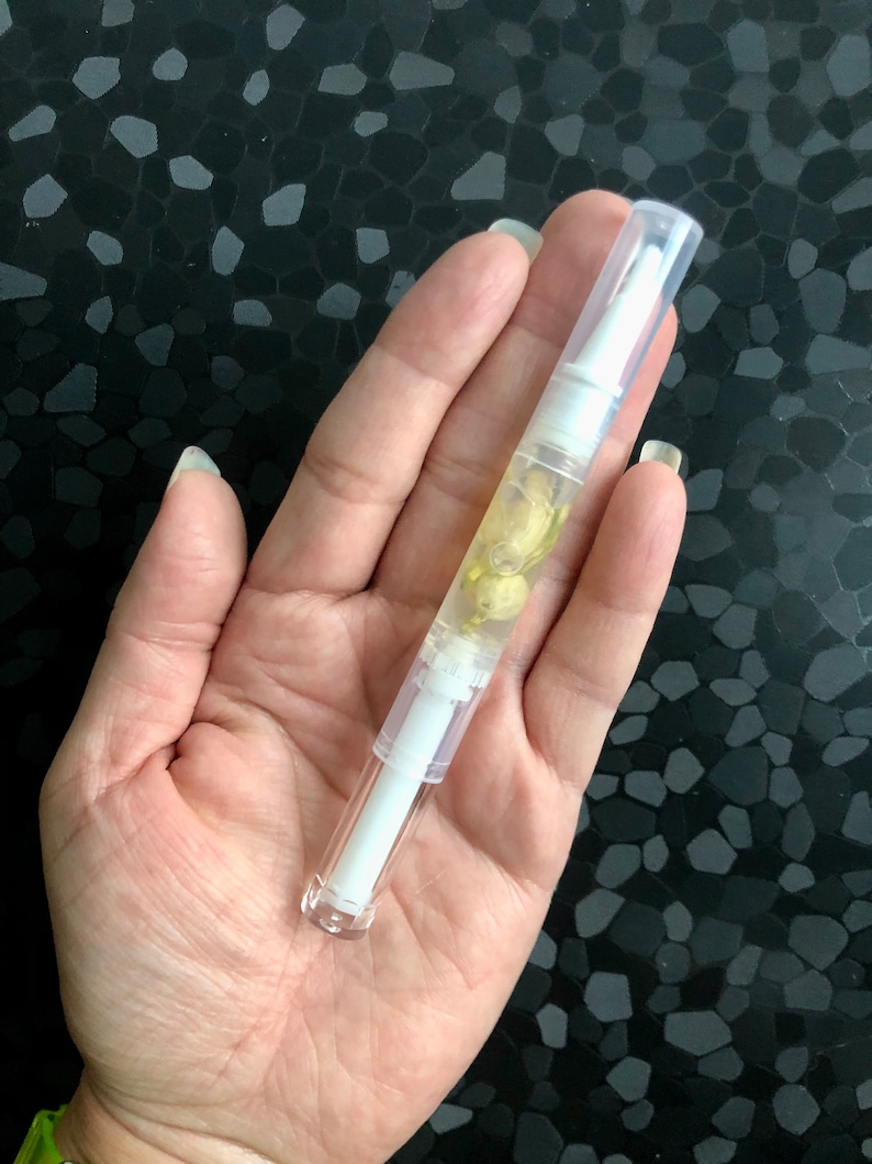 Peut inclure: Un tube en plastique transparent avec un bouchon blanc et un liquide jaune &agrave; l'int&eacute;rieur. Le tube est rempli de petites fleurs blanches.