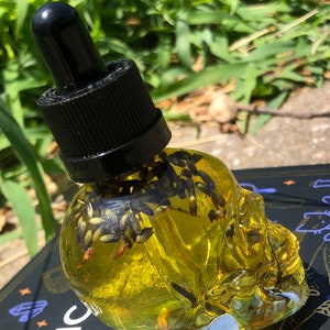 Peut inclure: Une bouteille en verre transparente en forme de cr&acirc;ne remplie d'un liquide jaune et de fleurs de lavande s&eacute;ch&eacute;es. La bouteille est munie d'un bouchon compte-gouttes noir.