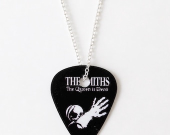 May include: Black guitar pick pendant with a silver chain. The pick features the band name "The Smiths" and the album title "The Queen is Dead" in white text, along with a white graphic of a skull and hand.