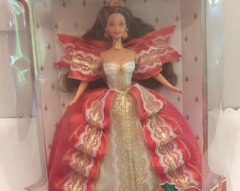 May include: A Barbie doll in a clear plastic box. The doll is wearing a red and gold gown with white lace accents. The box has the words "Happy Holidays" and "Barbie Special Edition" printed on it.