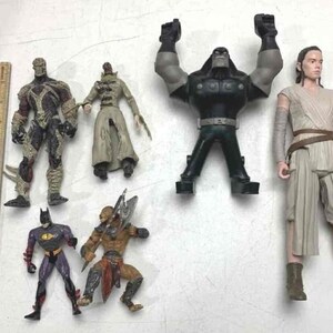 Puede incluir: Colección de figuras de acción, incluyendo personajes de cómics y películas. Figuras como Spawn, Batman y un personaje de Star Wars. También hay una regla de madera.