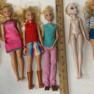 May include: A collection of six dolls with different hairstyles and outfits. The dolls are wearing a variety of clothing, including a pink dress with a leopard print, a pink dress with a white stripe, a red vest with a rainbow skirt, a turquoise shirt with pink pants, a white shirt with blue shorts, and a nude dress.