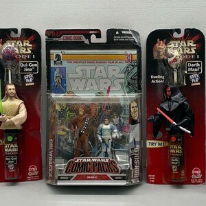 Könnte beinhalten: Eine Sammlung von Star Wars Spielzeug, darunter Actionfiguren, ein Comic und eine heiße Schokoladen Tasse. Die Spielzeuge zeigen Charaktere aus dem Star Wars Episode I: Die Phantomen Menace Film, darunter Qui-Gon Jinn, Darth Maul und Chewbacca.