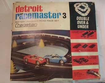 May include: A vintage Detroit Racemaster 3 battery-powered road race set with two cars, a blue car and a red car, on a track with a double over and under design. The box features the Cragstan logo and instructions for the set.