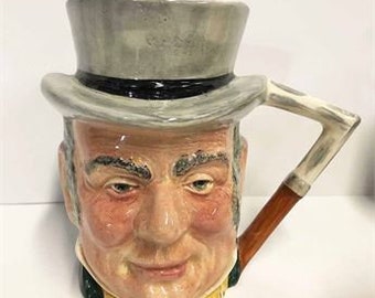 May include: A ceramic mug shaped like a man's head wearing a gray top hat and a bow tie. The mug has a brown handle shaped like a pipe.