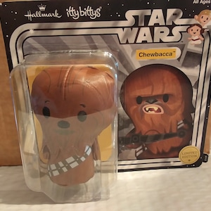 Op de afbeelding: Een bruin Chewbacca pluche speelgoed uit de Star Wars-franchise. Het speelgoed is verpakt in een doorzichtige plastic verpakking met een kartonnen achterkant. De verpakking heeft het Star Wars-logo en de woorden "Chewbacca" en "Limited Edition".