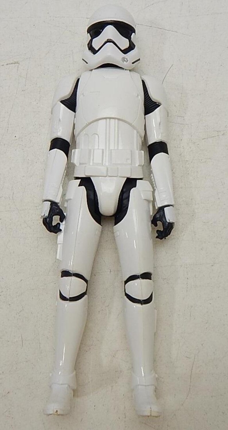 May include: A white and black Star Wars Stormtrooper action figure. The figure is standing with its arms at its sides. The figure has a black visor and a white helmet.