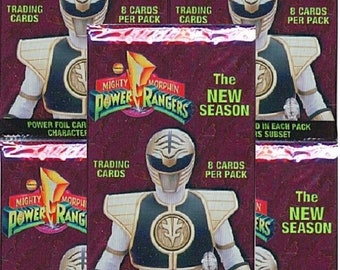 May include: Six packs of Mighty Morphin Power Rangers trading cards featuring the White Ranger. Each pack contains 8 cards and a foil card of a Power Ranger character. The packs are purple with gold and white accents. The text on the packs reads "The New Season".
