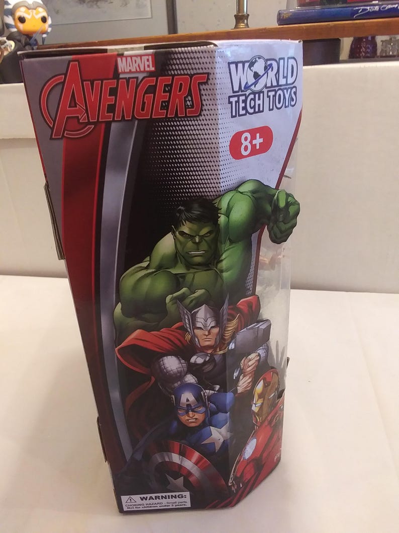 May include: A red, white and black box with the Marvel Avengers logo and the World Tech Toys logo. The box features images of Hulk, Thor, Captain America and Iron Man. The box is labelled 8+ and has a warning label.
