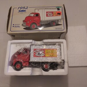 May include: A red 1952 GMC die-cast model truck with a white trailer, packaged in a box. The trailer has the text "The Nation's Largest Hardware Chain". The box features an illustration of the truck.