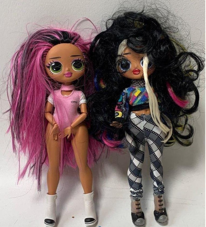 May include: Two fashion dolls with long, colorful hair. One doll has pink and black hair and is wearing a pink and white outfit with the word "OMG" on it. The other doll has black and white hair and is wearing a black and white checkered outfit with a rainbow shirt.