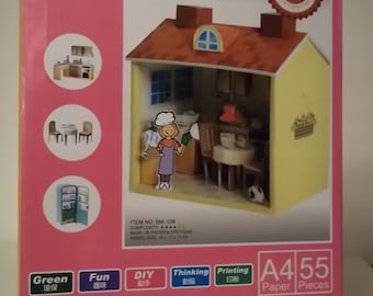 May include: A pink box with a yellow and red 3D paper model of a mini kitchen. The box has the words "Mini Kitchen" and "A4 55 Paper Pieces" on it. The box also has a picture of a woman in a chef's hat standing in the kitchen.