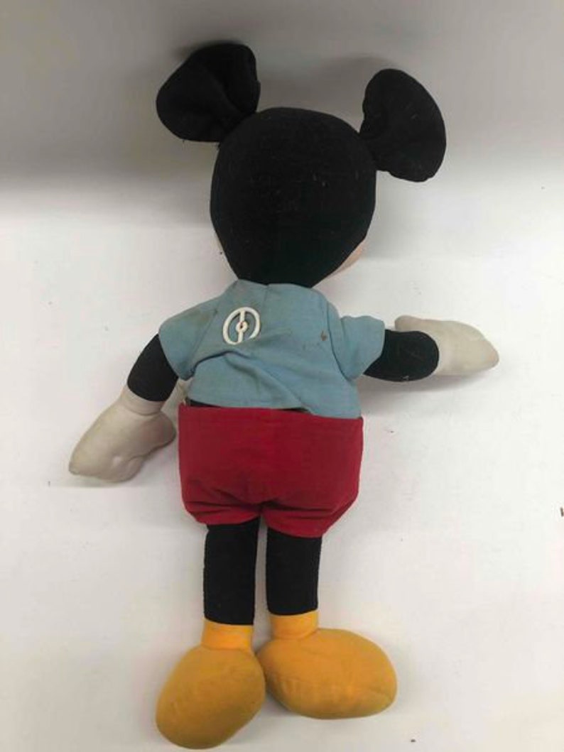 Puede incluir: Un juguete de peluche vintage de Mickey Mouse con orejas negras, cabeza negra, camisa azul con un c&iacute;rculo blanco, pantalones cortos rojos y zapatos amarillos.