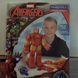 K&ouml;nnte beinhalten: Ein Iron Man-Charakter aus Papier zum Zusammenbauen aus der Avengers-Serie. Die Box zeigt das Avengers-Logo, das Marvel-Logo und den Text "AGES 6+". Die zusammengebaute Figur ist 30.48 cm gro&szlig;. Die Box enth&auml;lt auch den Text "EASY TO ASSEMBLE".