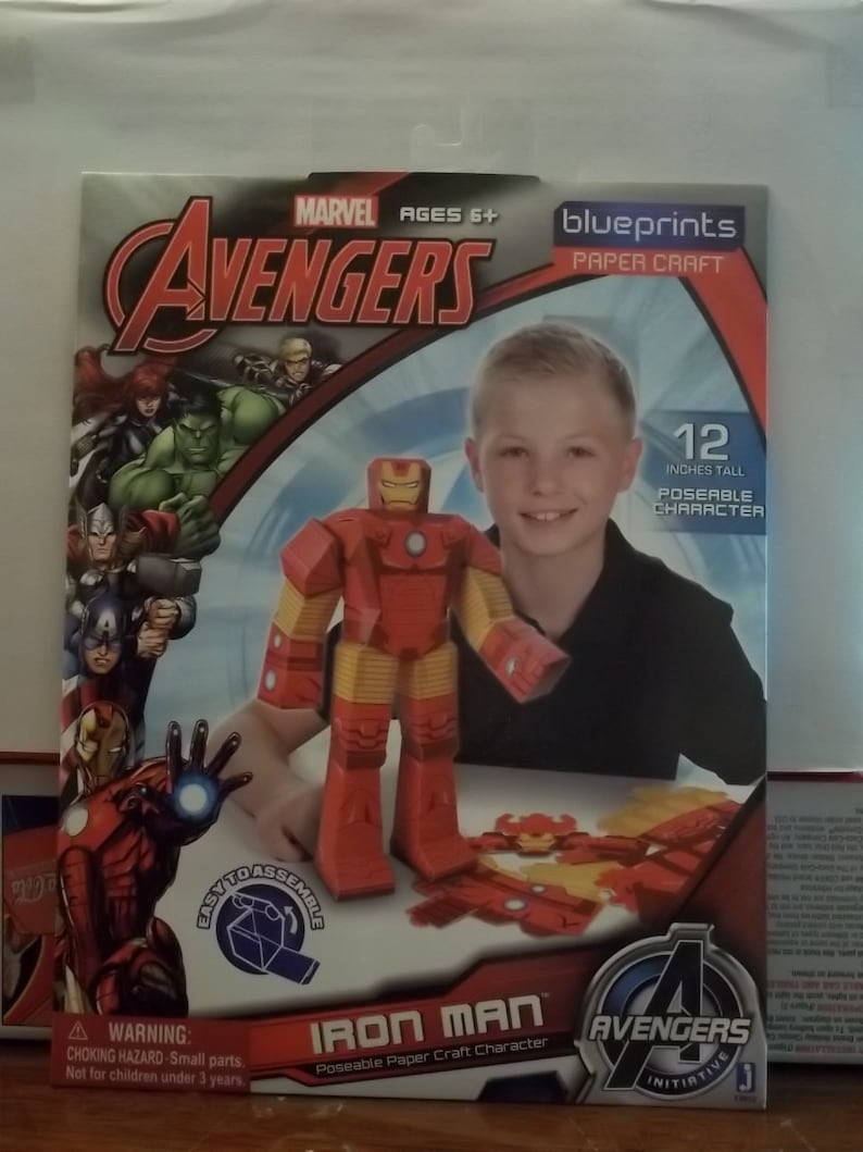 K&ouml;nnte beinhalten: Ein Iron Man-Charakter aus Papier zum Zusammenbauen aus der Avengers-Serie. Die Box zeigt das Avengers-Logo, das Marvel-Logo und den Text "AGES 6+". Die zusammengebaute Figur ist 30.48 cm gro&szlig;. Die Box enth&auml;lt auch den Text "EASY TO ASSEMBLE".