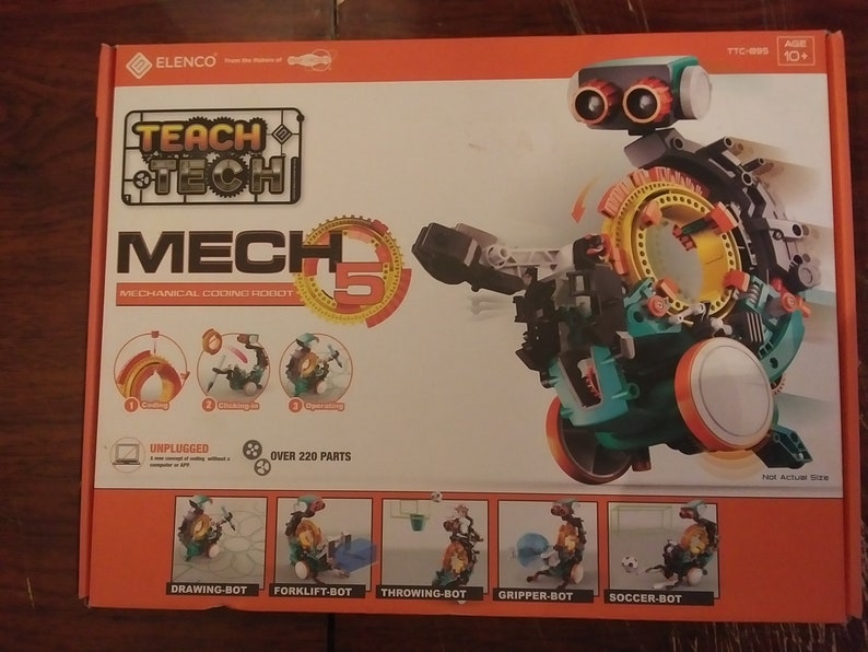 Puede incluir: Un kit de robot de codificaci&oacute;n mec&aacute;nica Teach Tech Mech 5 con m&aacute;s de 220 piezas. El robot es azul, verde, negro y naranja. La caja muestra el robot en diferentes configuraciones, incluyendo dibujo, carretilla elevadora, lanzamiento, agarre y f&uacute;tbol.