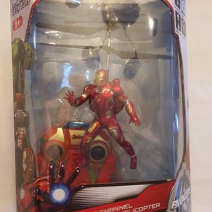 May include: A red and gold Iron Man flying figure infrared helicopter toy in a clear plastic box. The box has the words "Iron Man 2 Channel Flying Figure Infrared Helicopter" on the front. The box also has the Avengers logo on the side.