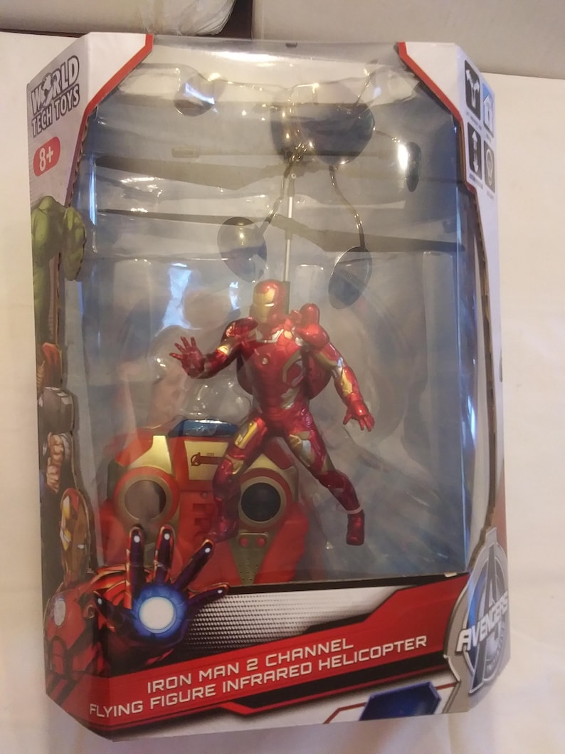 May include: A red and gold Iron Man flying figure infrared helicopter toy in a clear plastic box. The box has the words "Iron Man 2 Channel Flying Figure Infrared Helicopter" on the front. The box also has the Avengers logo on the side.