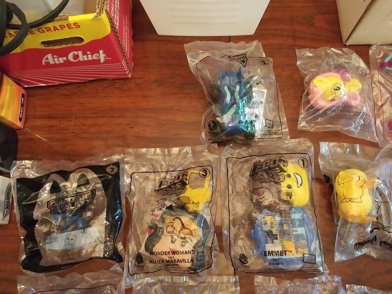Puede incluir: Una colecci&oacute;n de bolsas de pl&aacute;stico que contienen peque&ntilde;os juguetes de la pel&iacute;cula Lego 2. Los juguetes son de varios colores, incluyendo azul, amarillo y rojo. Las bolsas est&aacute;n etiquetadas con los nombres de los personajes, incluyendo Wonder Woman, Emmet y Unikitty.