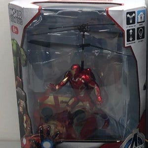 May include: A red and gold Iron Man action figure in a helicopter toy. The helicopter has a clear plastic casing and a black rotor. The box has the words "Avengers" and "World Tech Toys" on it.