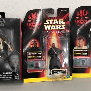 Puede incluir: Tres paquetes de figuras de acción de Star Wars. El primer paquete es un paquete plateado y negro con una imagen de Han Solo. El segundo paquete es un paquete rojo, negro y blanco con una imagen de Darth Maul. El tercer paquete es un paquete rojo, negro y blanco con una imagen de un personaje de Star Wars Episodio I. Los paquetes tienen todos las palabras "Star Wars" y "Episodio I" en ellos.