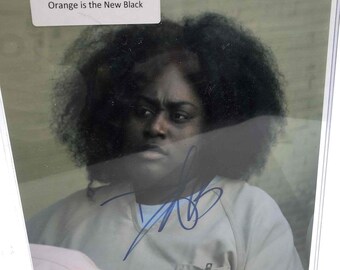 May include: A black and white photo of Danielle Brooks, an actress from the TV show Orange is the New Black, with her signature. The photo is framed and has a white mat.