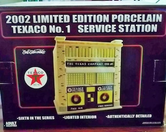 May include: A 2002 Limited Edition Porcelain Texaco No. 1 Service Station collectible. The model is a yellow and white building with a Texaco sign and a lighted interior. The box features a black background with the text "2002 Limited Edition Porcelain Texaco No. 1 Service Station" in white.