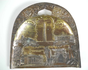 May include: An antique metal tray with a handle, featuring embossed images of Washington D.C. landmarks. The tray has a floral border and a central design with the Washington Monument. The color is a mix of gold and silver.