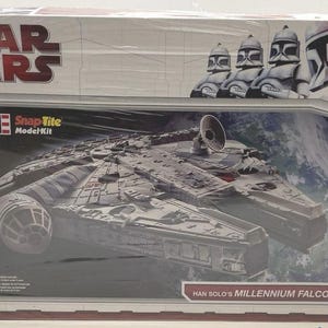 May include: A Star Wars Revell SnapTite model kit box featuring the Millennium Falcon spaceship. The box has the Star Wars logo and images of clone troopers. The text "Han Solo's Millennium Falcon" is also visible.