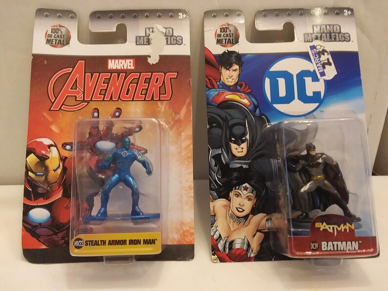 May include: Two Nano Metalfigs action figures, one Marvel Avengers Stealth Armor Iron Man and one DC Batman. The figures are in clear plastic packaging attached to colorful cardboard backings. The Marvel figure is blue, and the DC figure is black and gray.