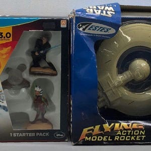 May include: Two Star Wars themed boxes. The box on the left is a Disney Infinity game for the Wii U console. The box on the right is an Estes model rocket kit for a Trade Federation Battleship.